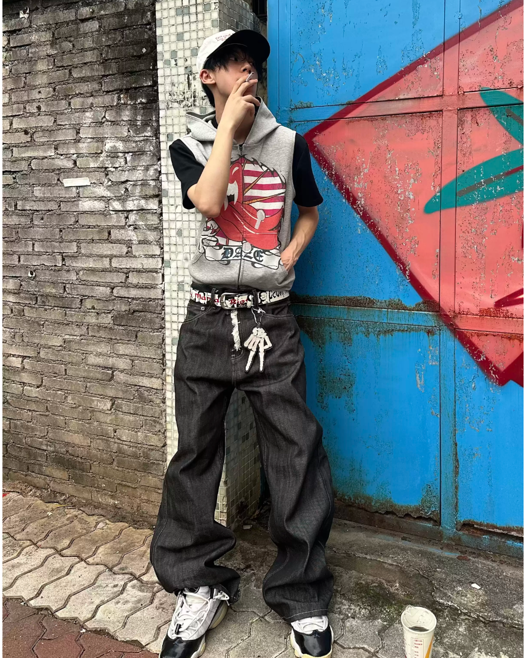 Person leaning against a textured wall with graffiti, wearing a gray hoodie and black pants.