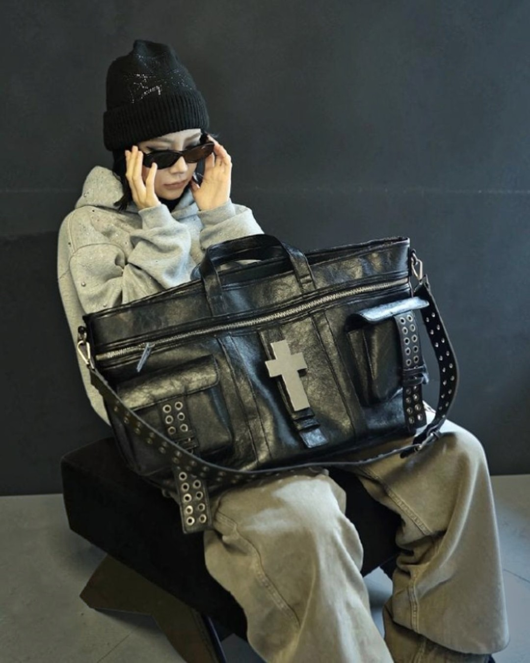 Black leather-look cross tote bag with front cross patch, stud trim, and side pouch