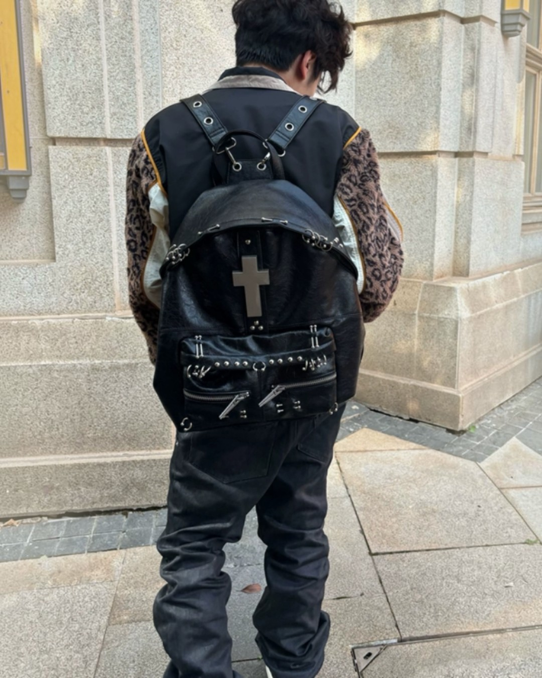 Black backpack with front cross panel, studded belt details, and padded straps