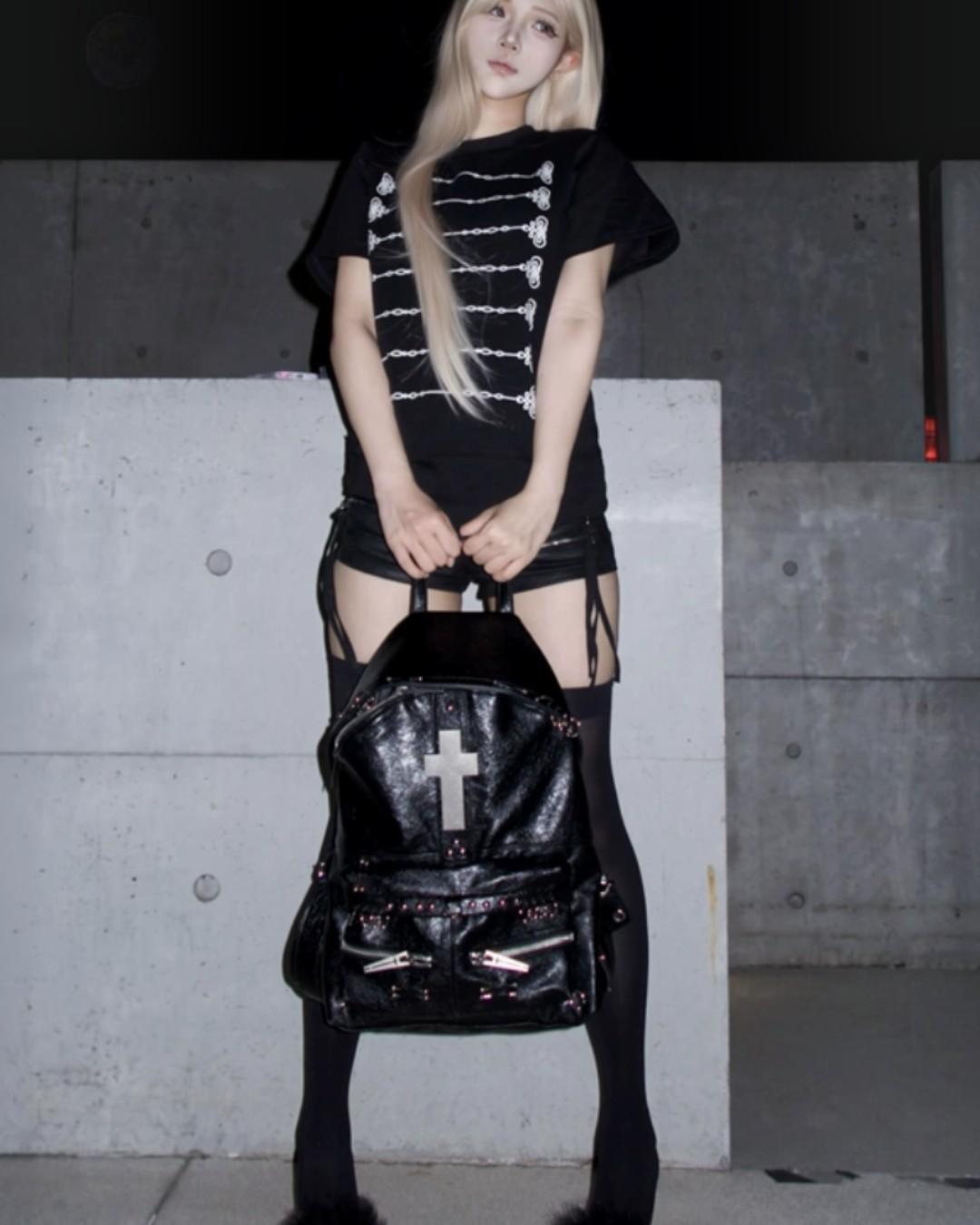 Black backpack with cross emblem, stud trim, and front zip compartments