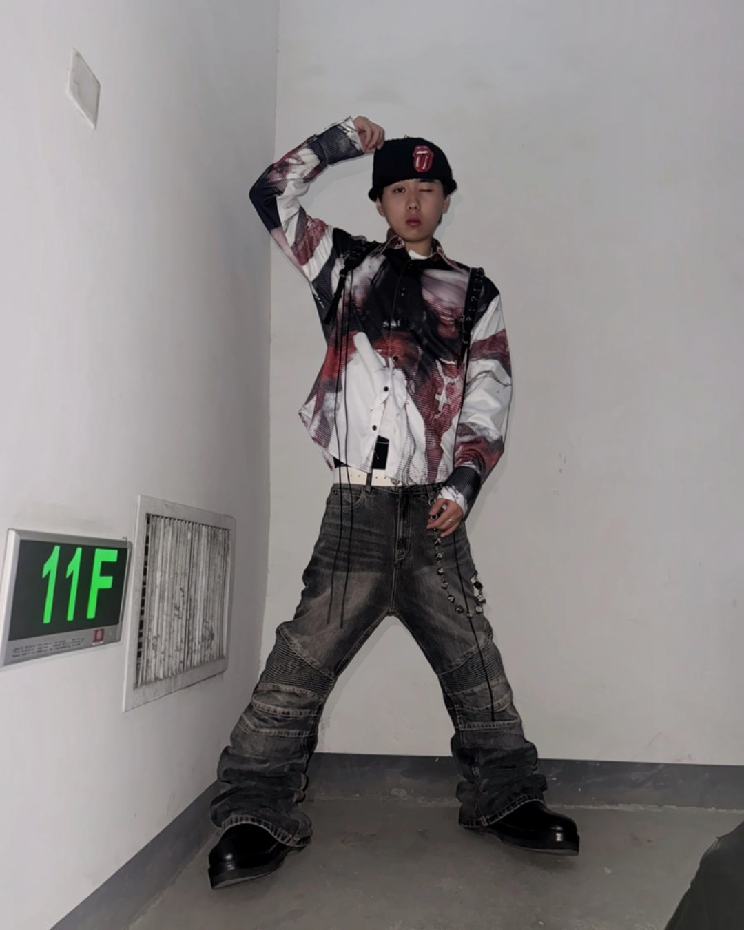 Person wearing a colorful jacket and plaid pants posing in a hallway with an '11F' sign.